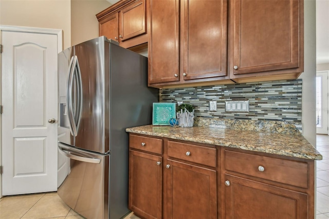 kitchen with backsplash, light stone countertops, light tile patterned flooring, and stainless steel refrigerator with ice dispenser