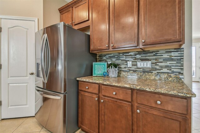 2212 Valterra Vista Way, Valrico, FL 33594 - kitchen with stainless steel refrigerator with ice dispenser, light tile patterned flooring, backsplash, stone counters, and brown cabinets