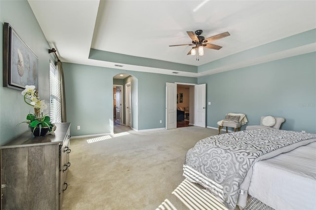 bedroom with light carpet, a raised ceiling, and ceiling fan