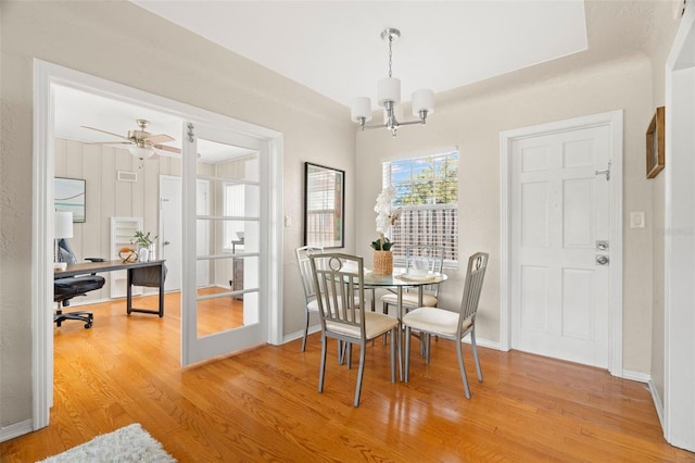 dining space with ceiling fan with notable chandelier and light hardwood / wood-style flooring