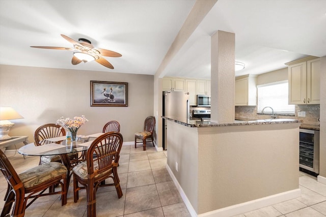 kitchen featuring cream cabinetry, appliances with stainless steel finishes, beverage cooler, and dark stone counters