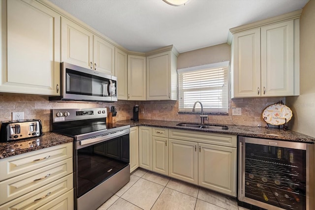 kitchen featuring dark stone counters, stainless steel appliances, beverage cooler, sink, and cream cabinets