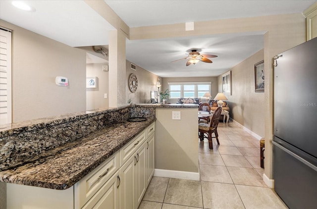 kitchen featuring kitchen peninsula, stainless steel fridge, dark stone counters, and cream cabinets