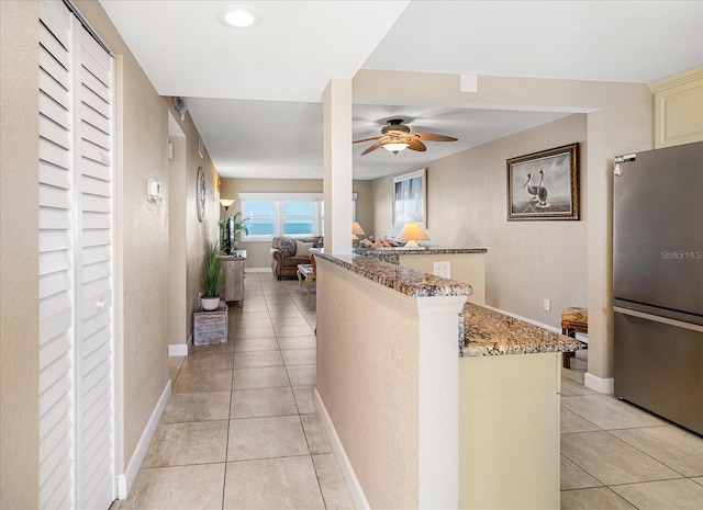 kitchen featuring ceiling fan, stainless steel fridge, dark stone countertops, light tile patterned floors, and kitchen peninsula