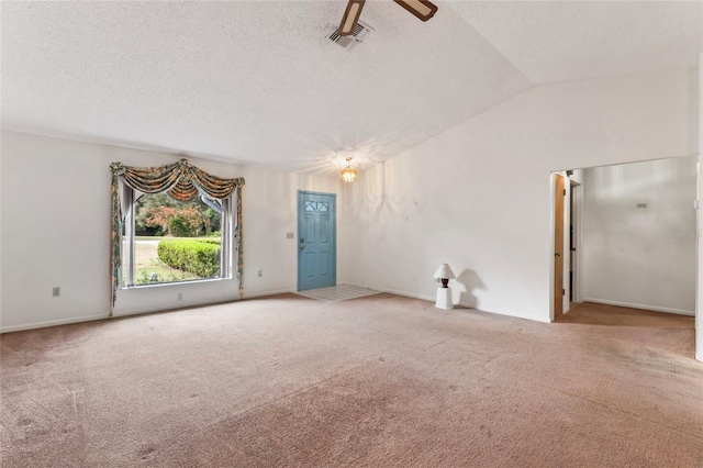 empty room featuring light carpet, a textured ceiling, and vaulted ceiling