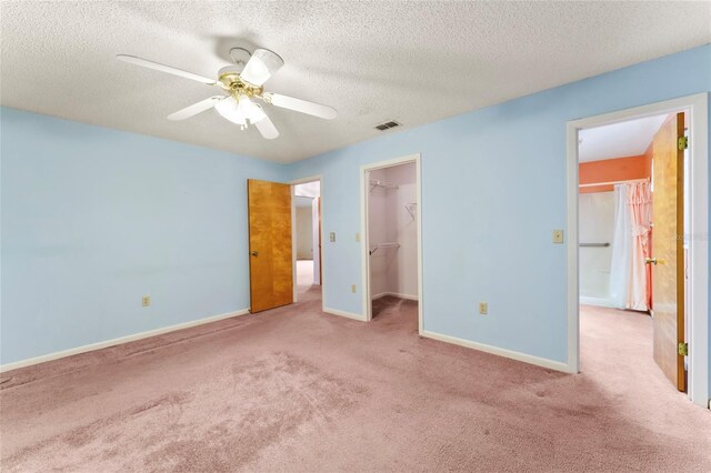 unfurnished bedroom featuring ceiling fan, a spacious closet, light carpet, and a closet