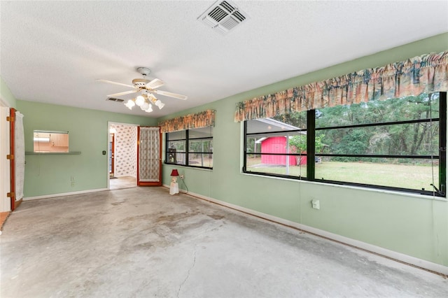 unfurnished room with concrete flooring, a textured ceiling, ceiling fan, and a healthy amount of sunlight