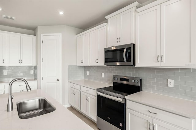 kitchen with appliances with stainless steel finishes, a sink, light countertops, white cabinets, and backsplash