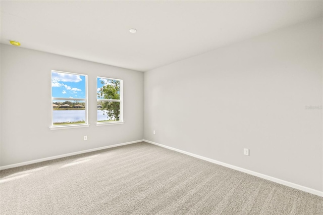 carpeted empty room featuring baseboards, a water view, and a smoke detector