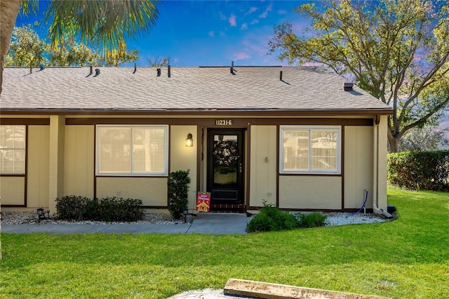 view of front of property featuring a front lawn, roof with shingles, and stucco siding