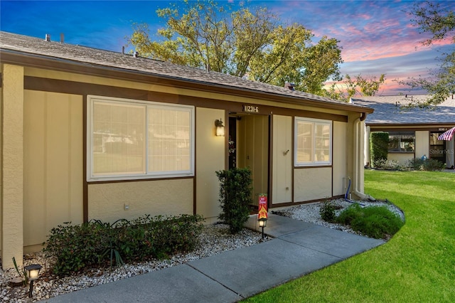 exterior entry at dusk with stucco siding and a yard