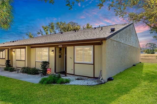 back of property featuring stucco siding, a shingled roof, and a yard