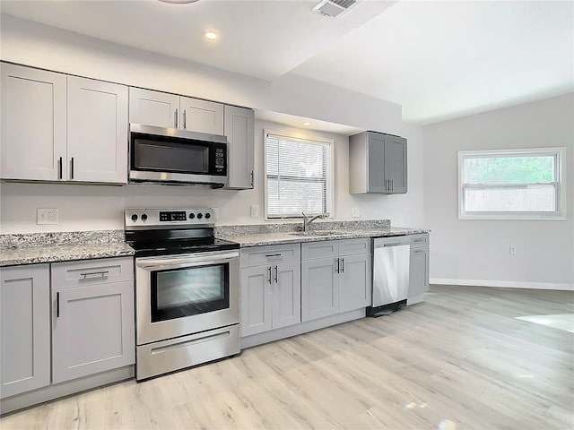 kitchen with gray cabinetry, sink, a wealth of natural light, appliances with stainless steel finishes, and light stone counters