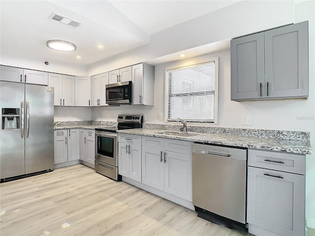 kitchen featuring gray cabinetry, light stone countertops, sink, light hardwood / wood-style floors, and appliances with stainless steel finishes