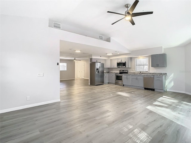 kitchen featuring gray cabinets, stainless steel appliances, vaulted ceiling, and light wood-type flooring