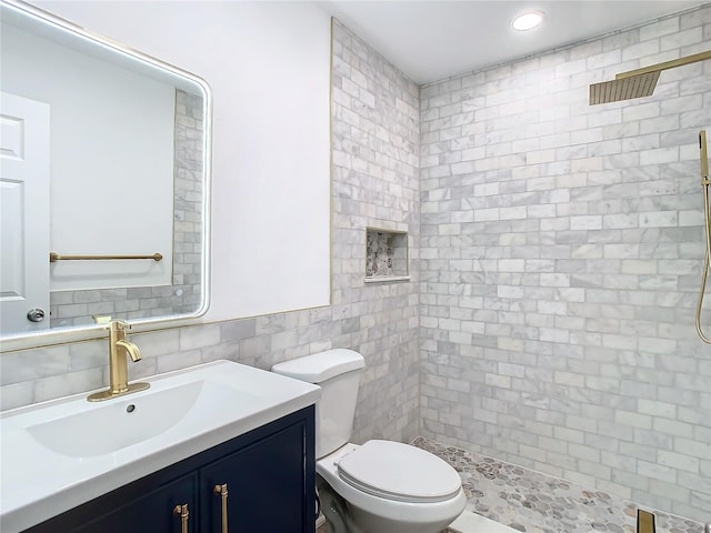 bathroom featuring tiled shower, vanity, toilet, and tile walls