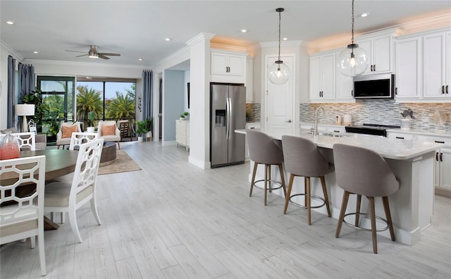 kitchen with a kitchen island with sink, sink, light wood-type flooring, white cabinetry, and stainless steel appliances