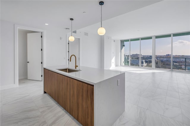 kitchen with floor to ceiling windows, pendant lighting, a kitchen island with sink, and sink