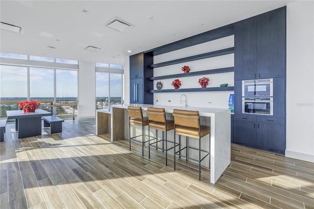 kitchen with a breakfast bar, a center island, expansive windows, sink, and light wood-type flooring