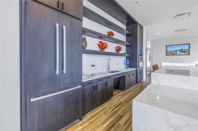 bar with light stone countertops, sink, wood-type flooring, and appliances with stainless steel finishes