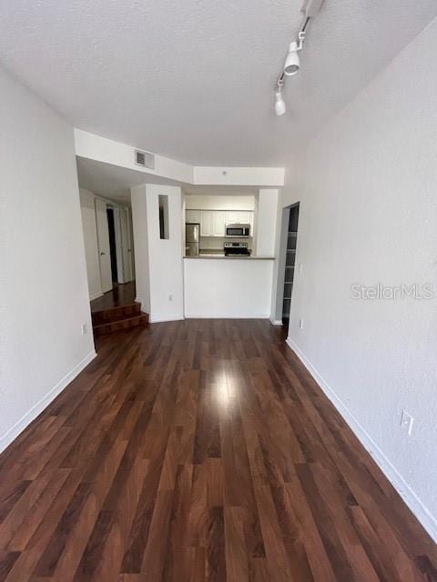 unfurnished living room with a textured ceiling, rail lighting, and dark hardwood / wood-style floors