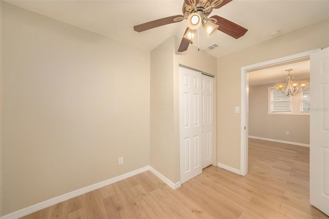 unfurnished bedroom with vaulted ceiling, a closet, ceiling fan with notable chandelier, and light wood-type flooring