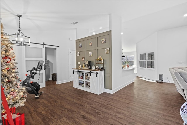 exercise room featuring a chandelier, a barn door, dark wood-type flooring, and vaulted ceiling