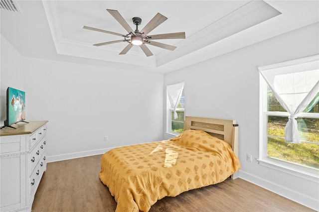 bedroom featuring multiple windows, wood-type flooring, a tray ceiling, and ceiling fan