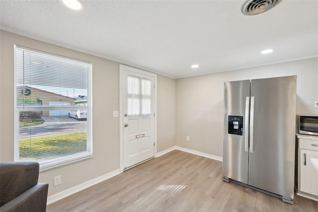 interior space with a textured ceiling, light wood-type flooring, stainless steel appliances, and a healthy amount of sunlight