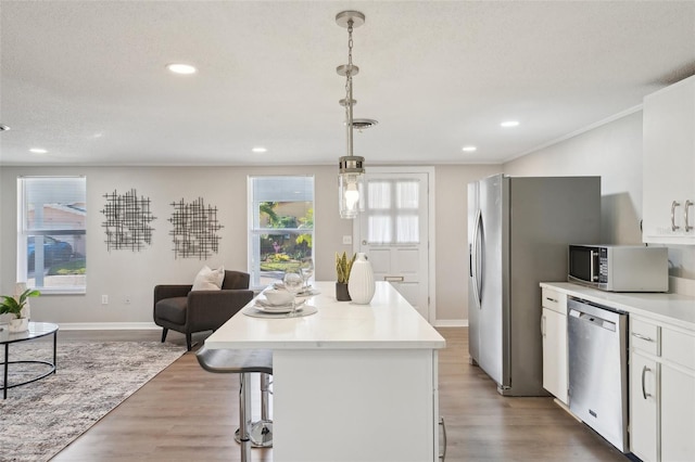 kitchen featuring stainless steel appliances, decorative light fixtures, white cabinets, hardwood / wood-style floors, and a kitchen island