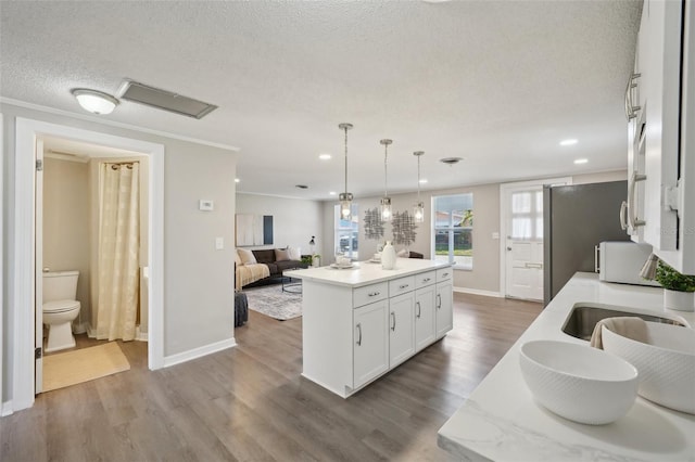 kitchen with a kitchen island with sink, hanging light fixtures, hardwood / wood-style flooring, a textured ceiling, and white cabinetry