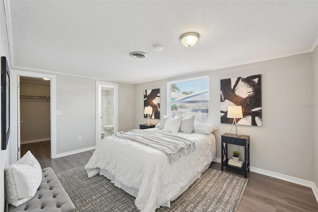 bedroom with ensuite bathroom, a textured ceiling, hardwood / wood-style flooring, a spacious closet, and a closet