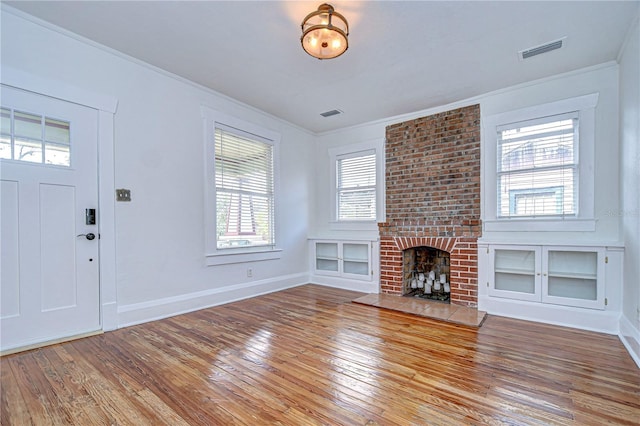 foyer entrance with hardwood / wood-style floors, a brick fireplace, a wealth of natural light, and crown molding