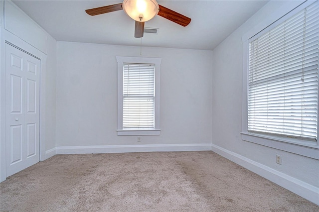 unfurnished room with light colored carpet, a wealth of natural light, and ceiling fan