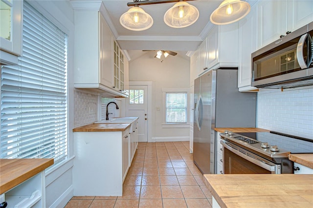 kitchen featuring appliances with stainless steel finishes, butcher block countertops, white cabinetry, hanging light fixtures, and lofted ceiling