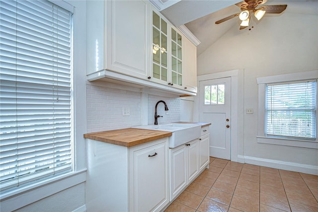 kitchen featuring wood counters, lofted ceiling, light tile patterned floors, tasteful backsplash, and white cabinetry