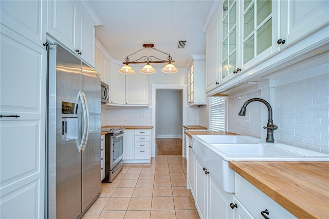 kitchen with hanging light fixtures, ornamental molding, butcher block countertops, white cabinetry, and stainless steel appliances