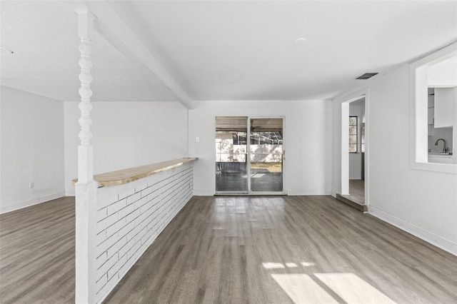 unfurnished living room with baseboards, wood finished floors, visible vents, and a sink