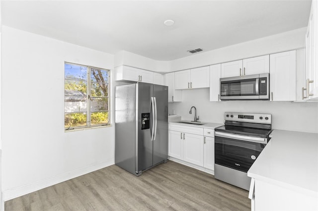 kitchen with light wood finished floors, visible vents, light countertops, appliances with stainless steel finishes, and a sink