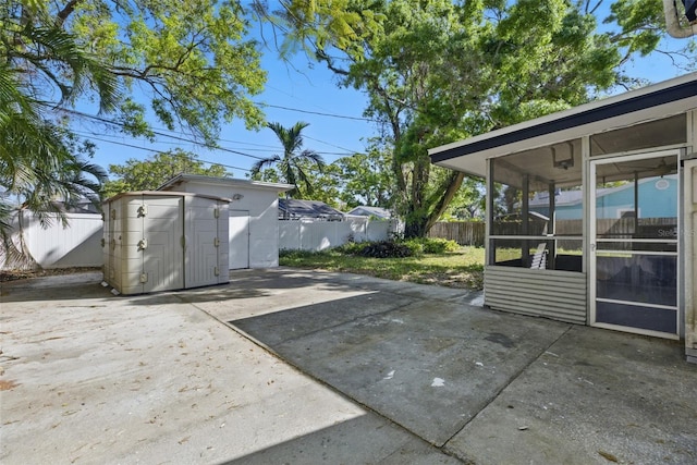 view of patio with a fenced backyard, a storage shed, an outdoor structure, and a sunroom