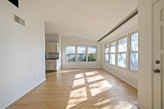 unfurnished living room featuring lofted ceiling, light hardwood / wood-style flooring, and a healthy amount of sunlight