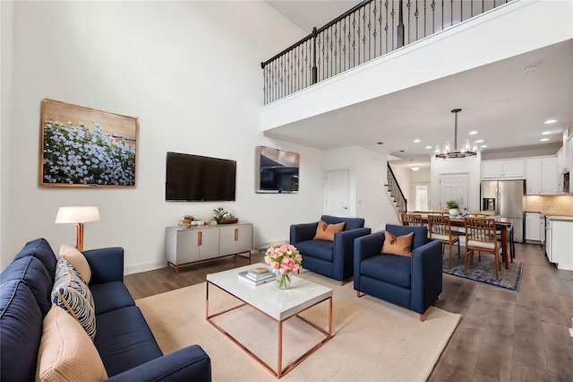 living room with a towering ceiling, an inviting chandelier, and dark wood-type flooring