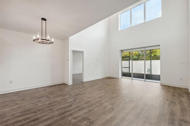 unfurnished living room with a towering ceiling, a chandelier, and dark hardwood / wood-style floors