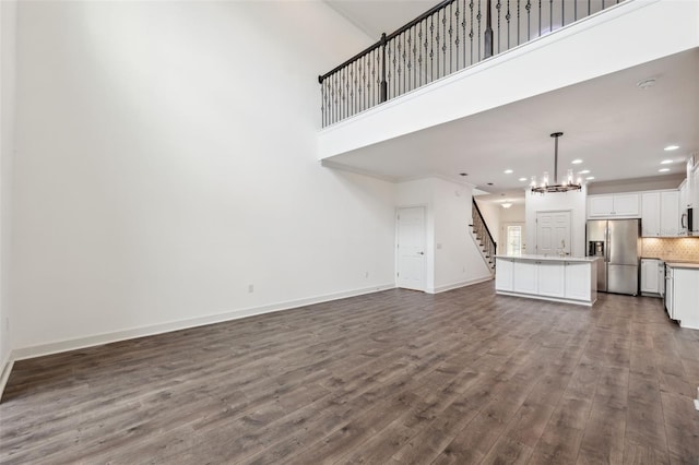 unfurnished living room featuring a notable chandelier, dark hardwood / wood-style floors, ornamental molding, and a high ceiling