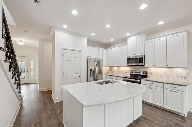 kitchen with white cabinetry, sink, stainless steel appliances, light stone counters, and an island with sink