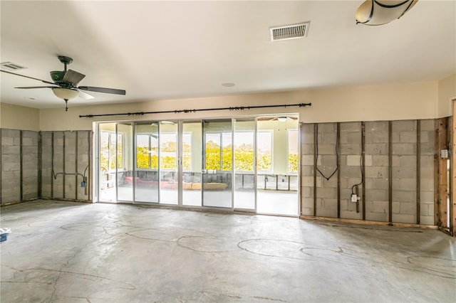 spare room with concrete flooring, concrete block wall, visible vents, and ceiling fan