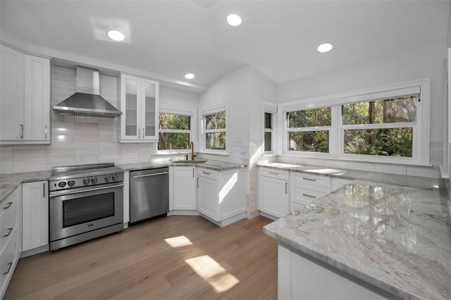 kitchen with white cabinetry, wall chimney range hood, backsplash, and appliances with stainless steel finishes