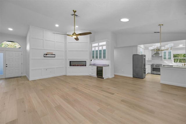 unfurnished living room with ceiling fan, light hardwood / wood-style flooring, beverage cooler, and lofted ceiling