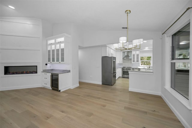 kitchen with white cabinets, appliances with stainless steel finishes, lofted ceiling, and wall chimney exhaust hood