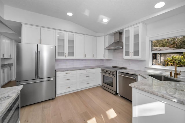 kitchen featuring sink, stainless steel appliances, wall chimney range hood, lofted ceiling, and white cabinets